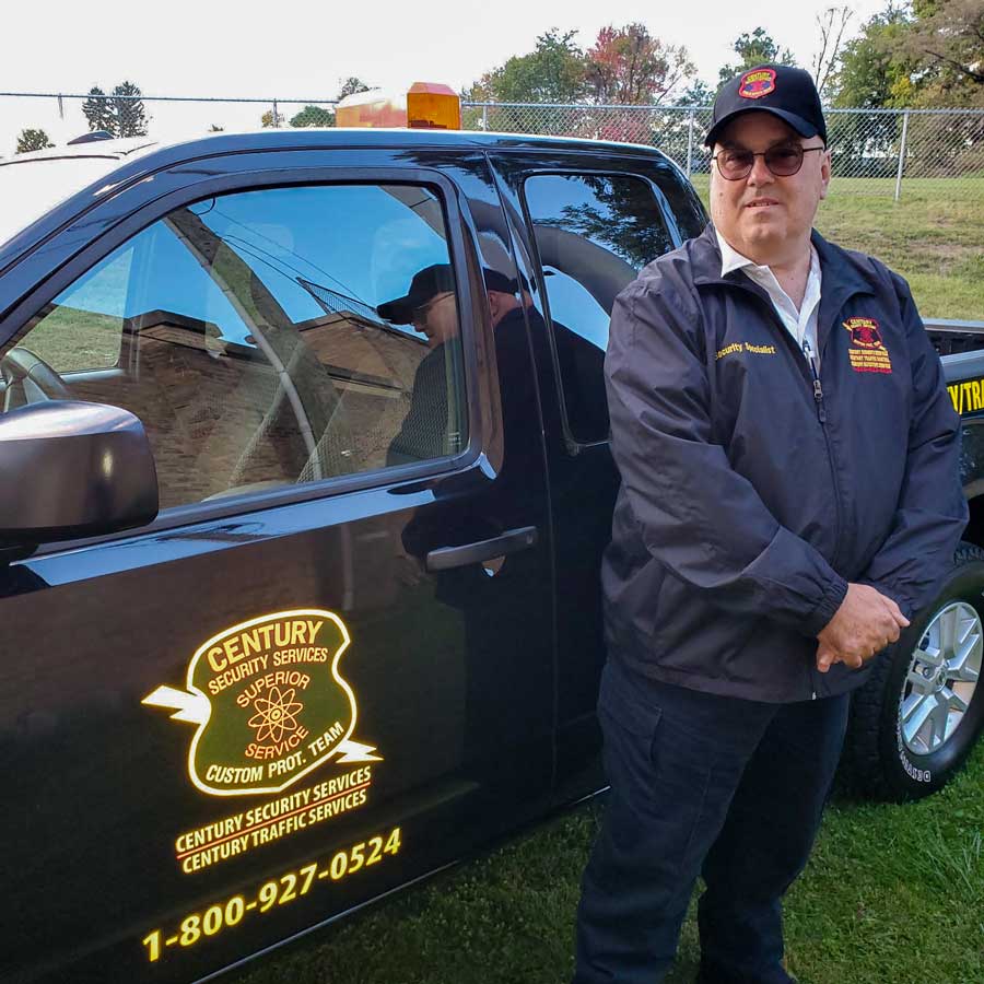 Male security guards stands outside his black Century Security vehicle.